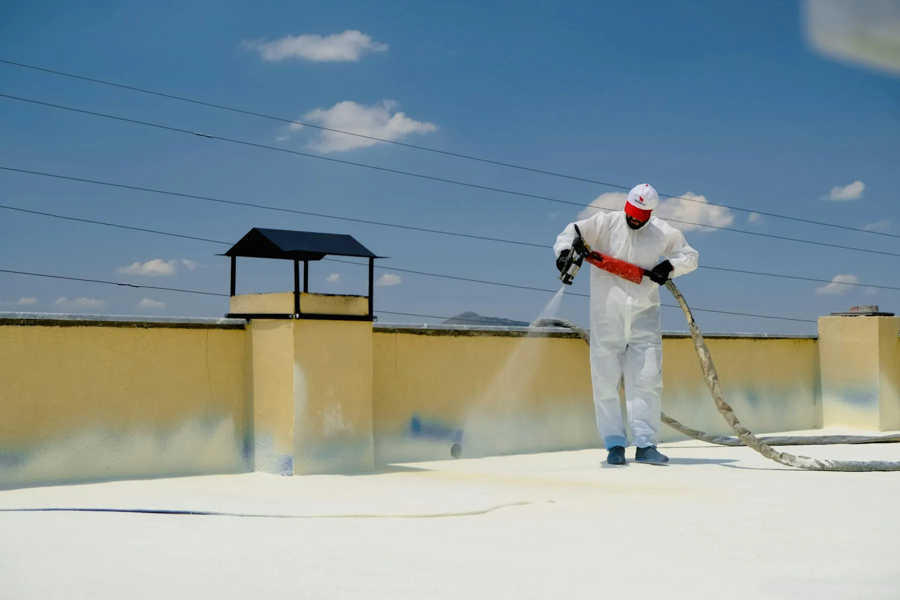 A waterproofer applying a coating to a flat concrete roof with parapet upstands