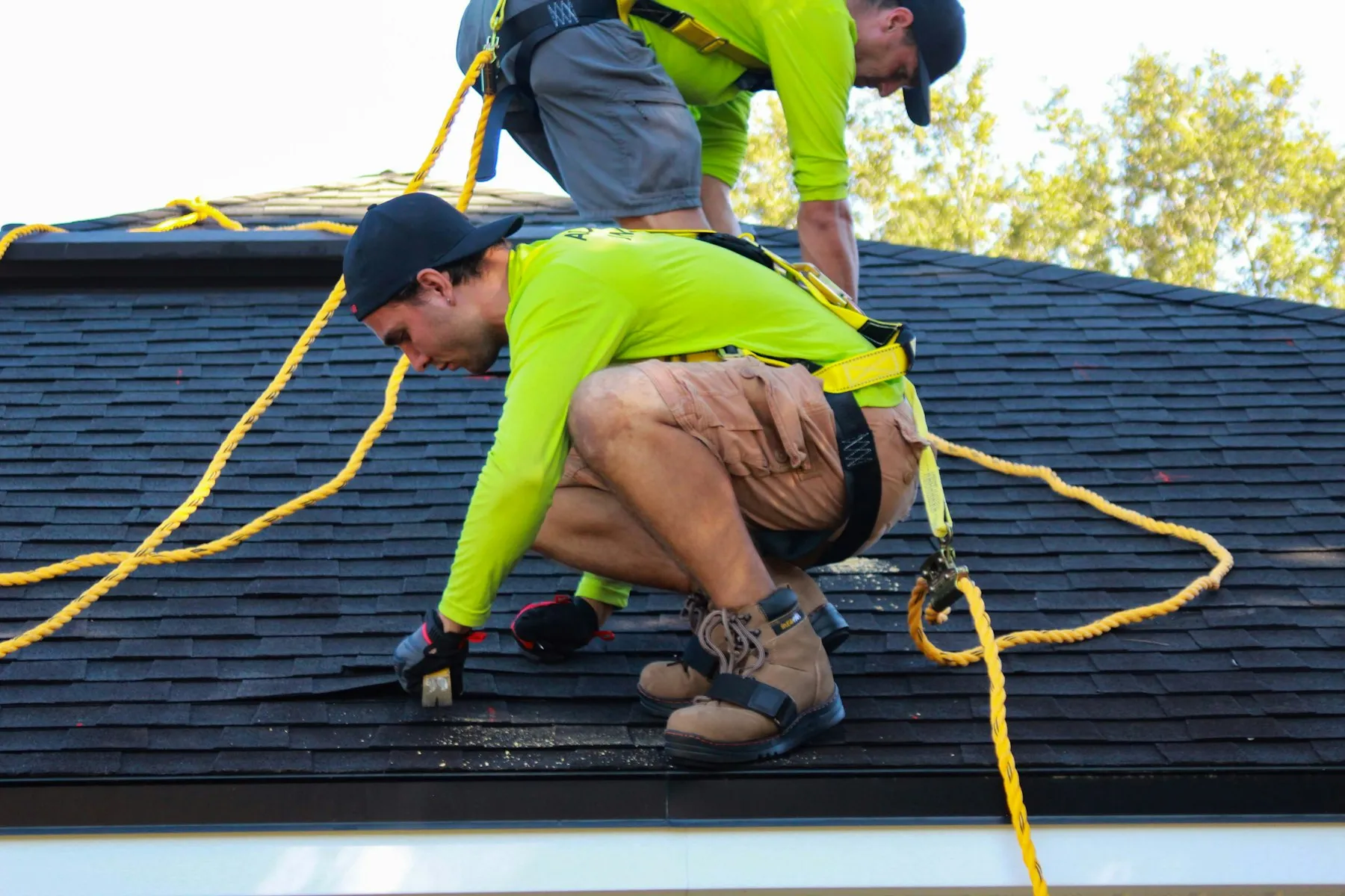 Two roofers working on a pitched roof wearing safety harnesses